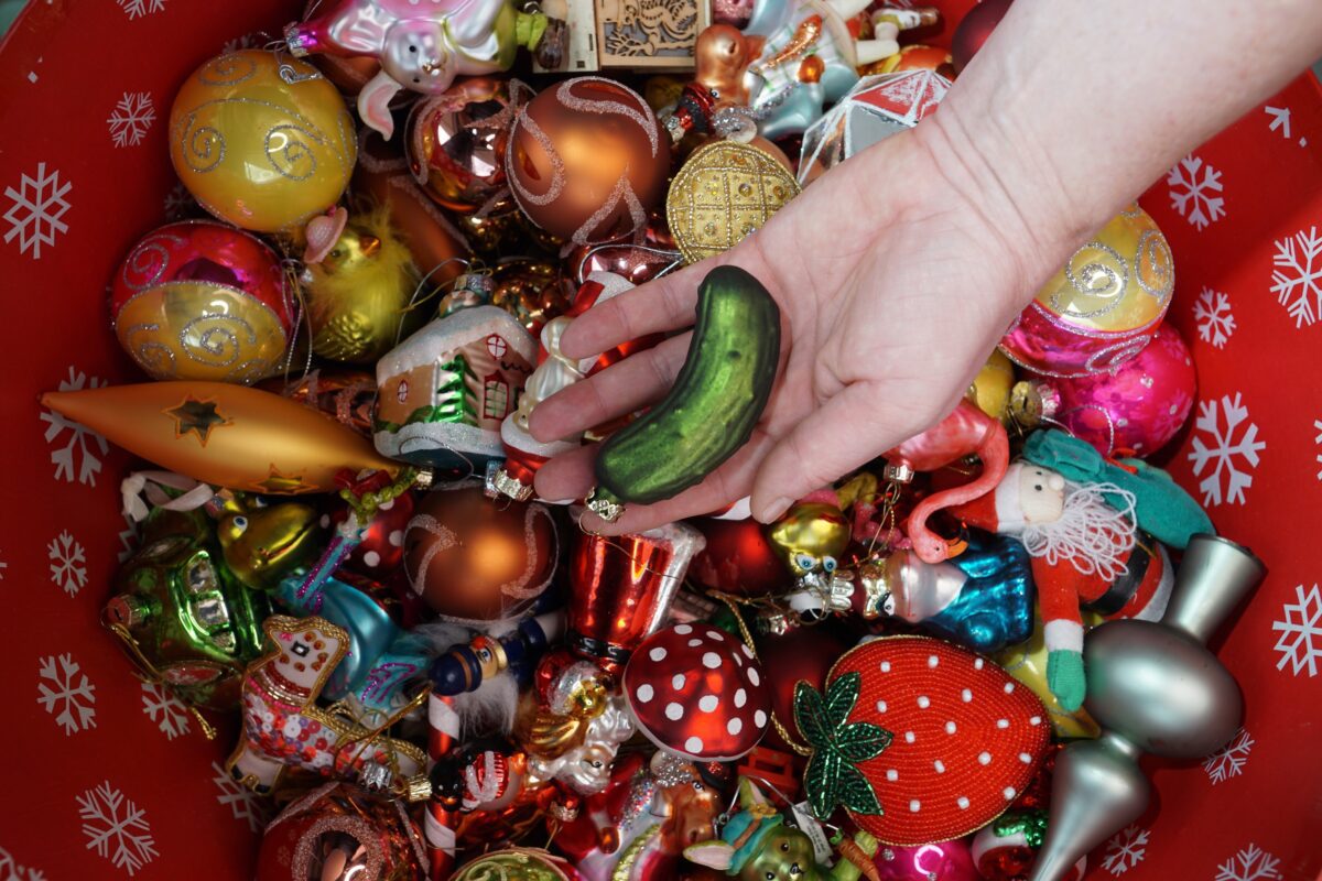 Woman's hand holding pickle ornament among many Christmas ornaments