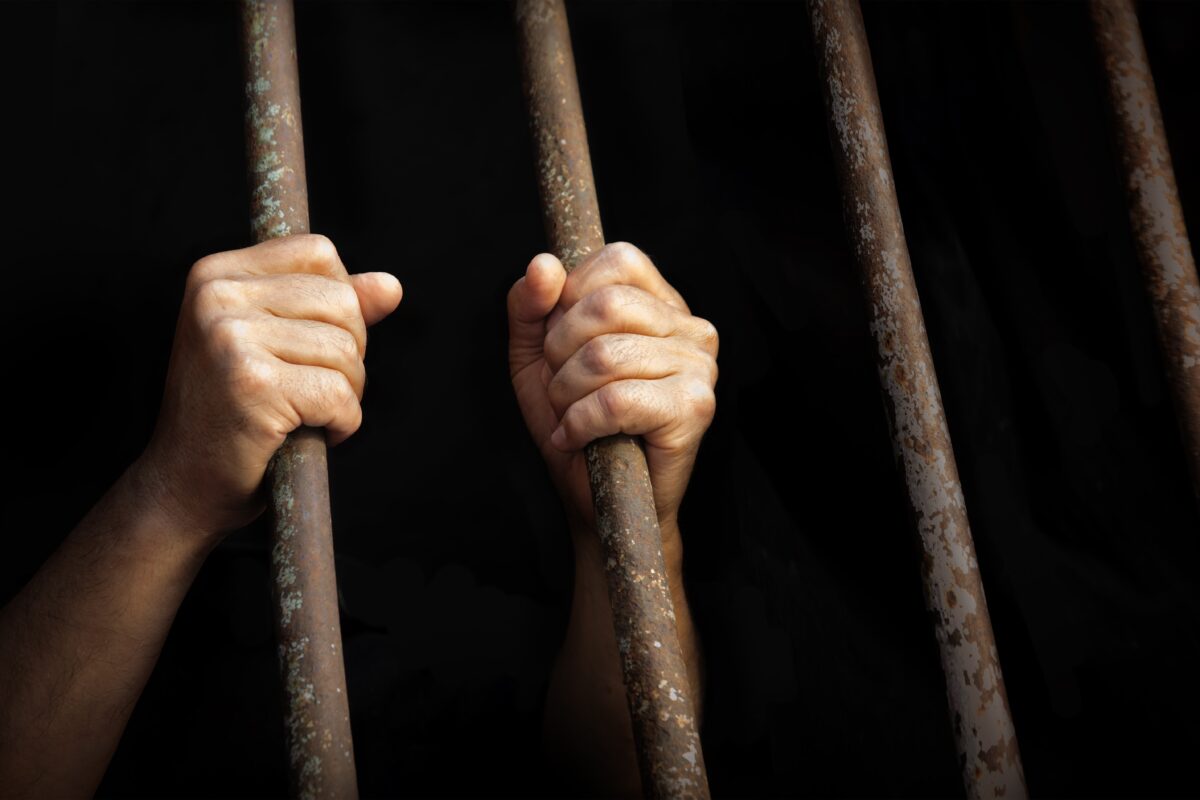 Man's hands holding prison bars