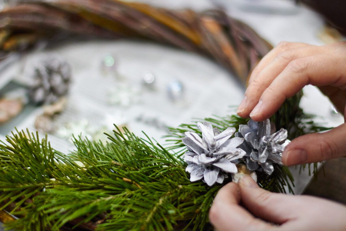 Woman's hands attaching pine cones to a wreath