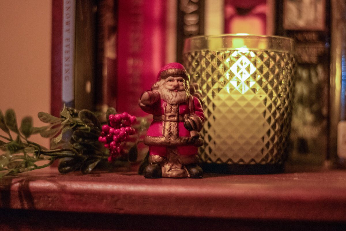 Old World Santa figurine next to a sprig of holly and a green votive
