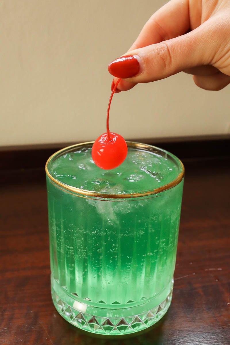 Woman's hand adding a cherry garnish to a cocktail