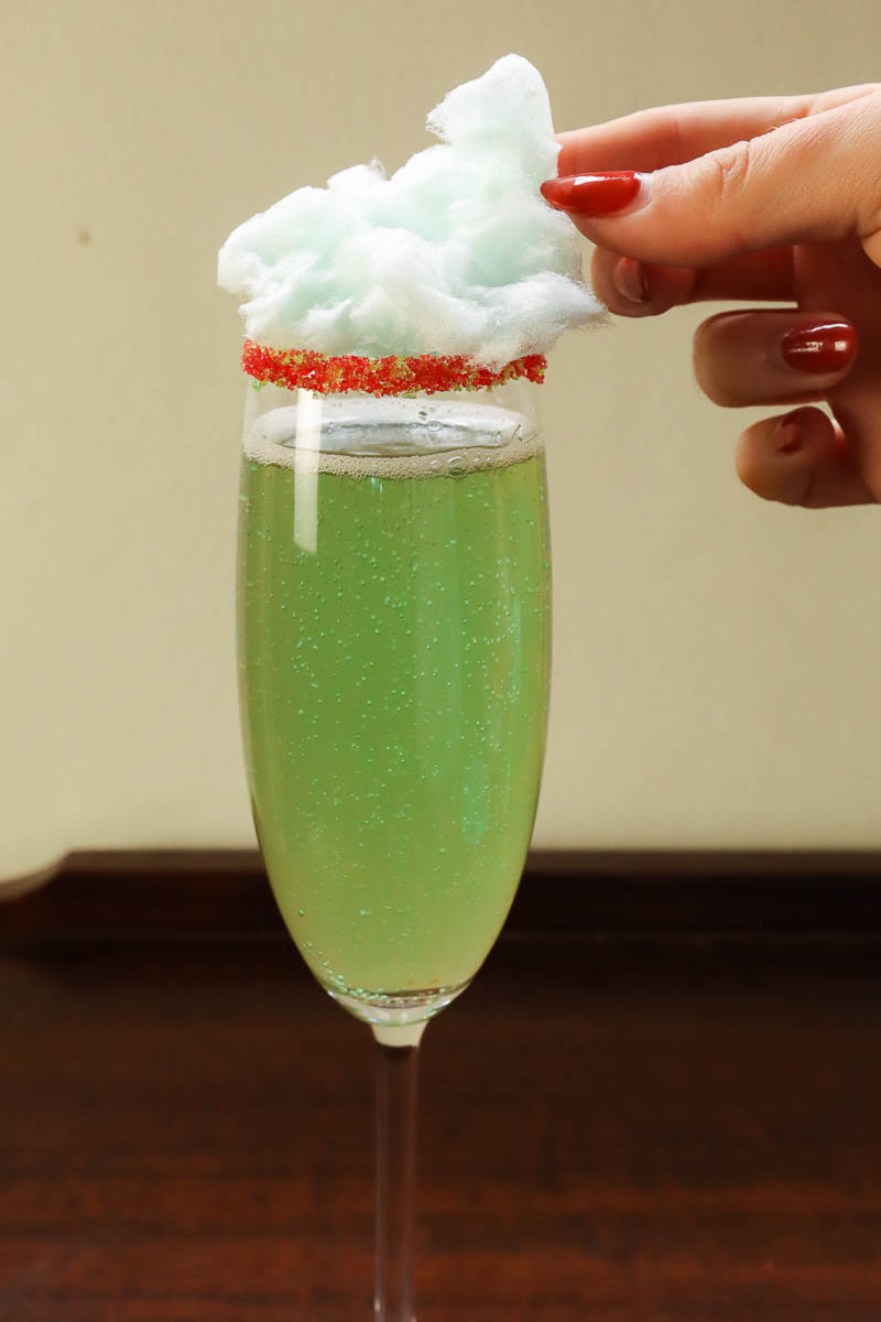 Woman's hand placing cotton candy garnish on champagne flute