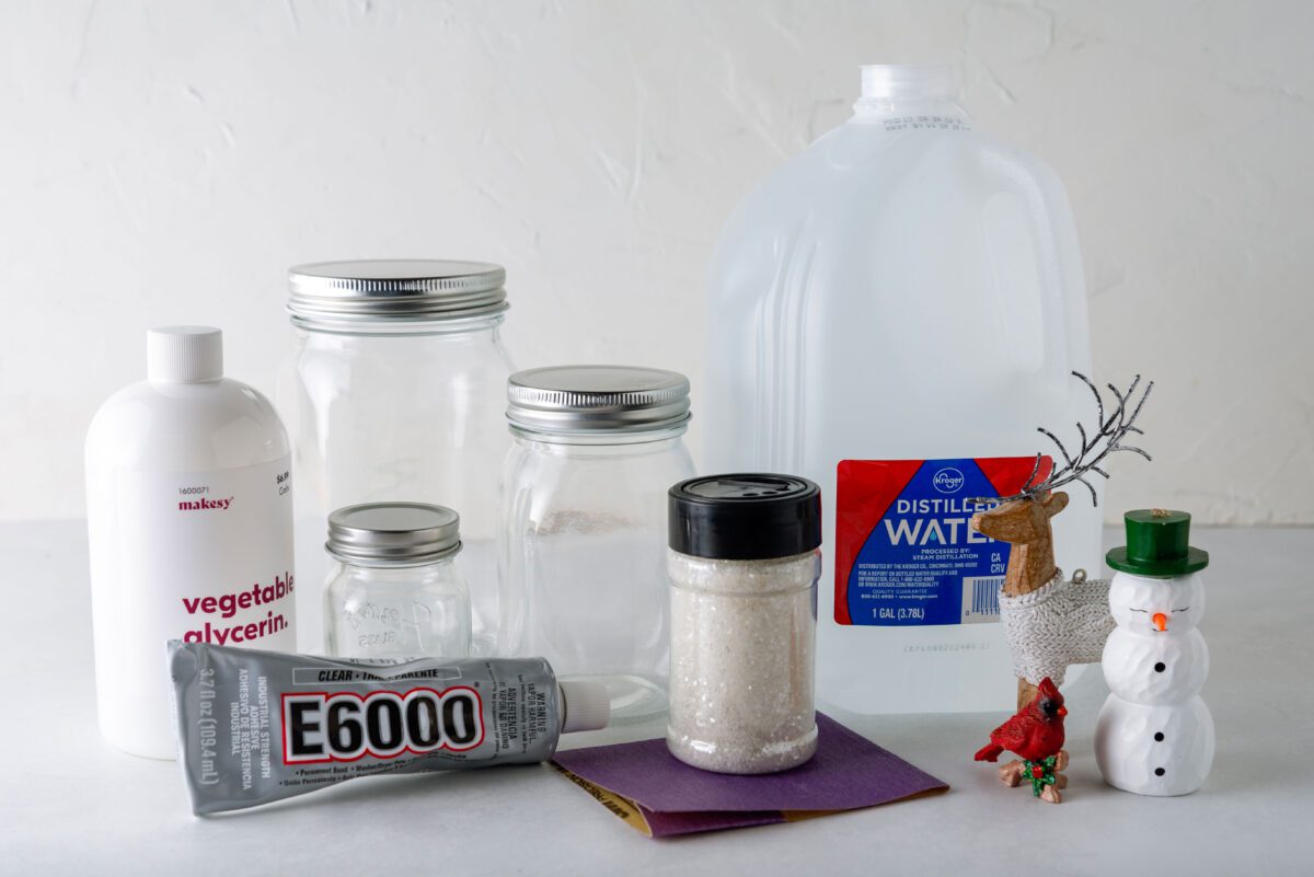 Materials for making a snow globe including jars, glycerin, glue, water, and figurines.