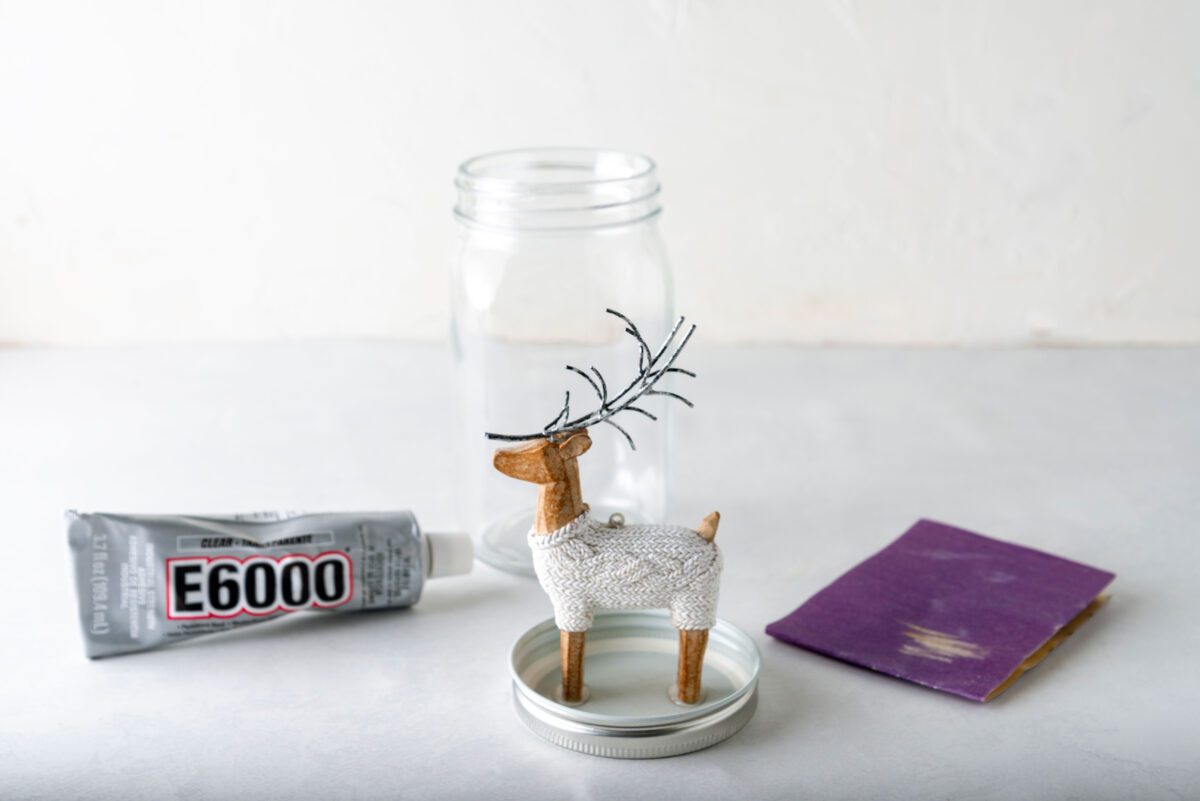 Step-by-step process of assembling a reindeer snow globe using glue and a jar lid.