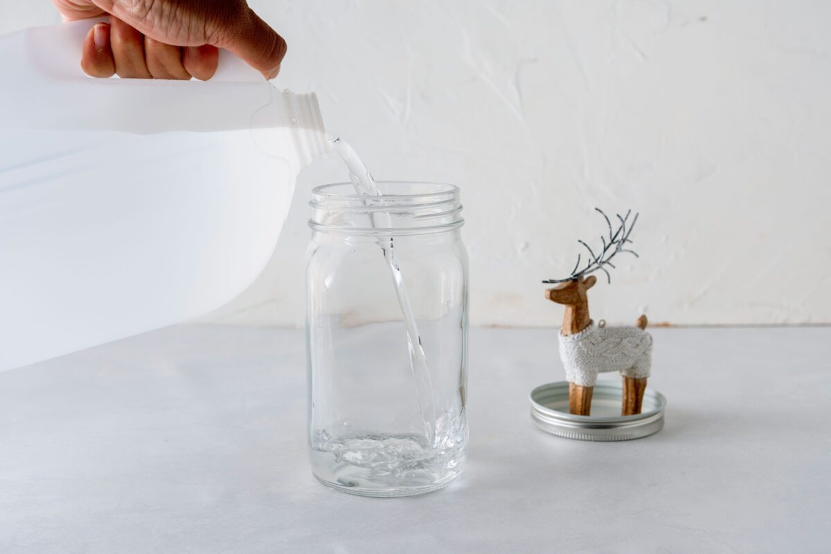 Pouring distilled water into an empty jar for a snow globe craft project.