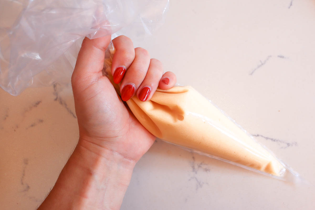 Hand holding piping bag filled with melted white chocolate. 