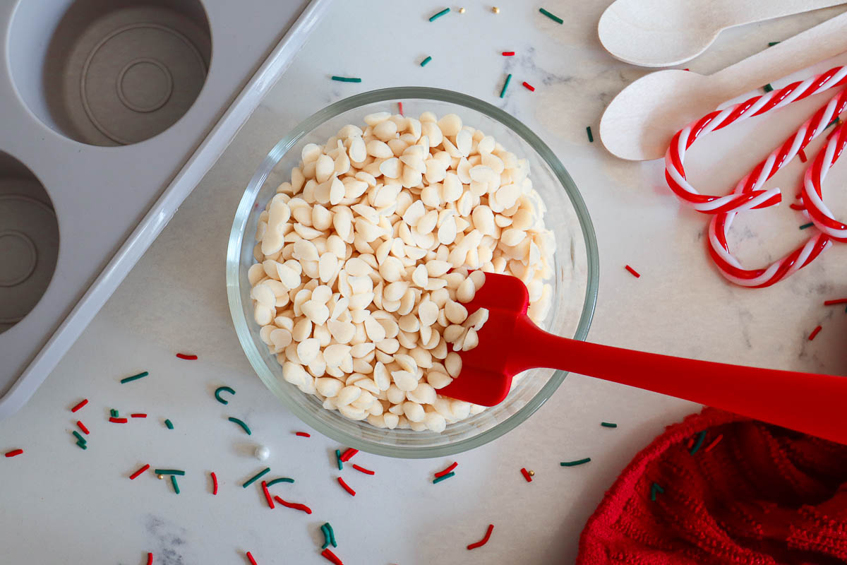 White chocolate chips in glass bowl with red spatula. 