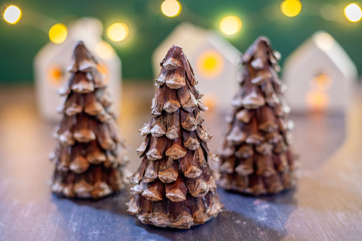 Decorative pine cone trees in foreground with fairy lights and mini houses.