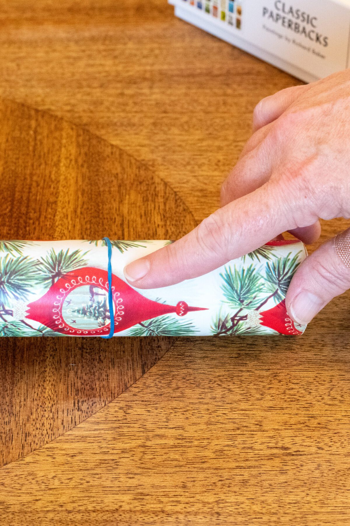 Woman's finger pointing to a rubber band on a roll of wrapping paper. 