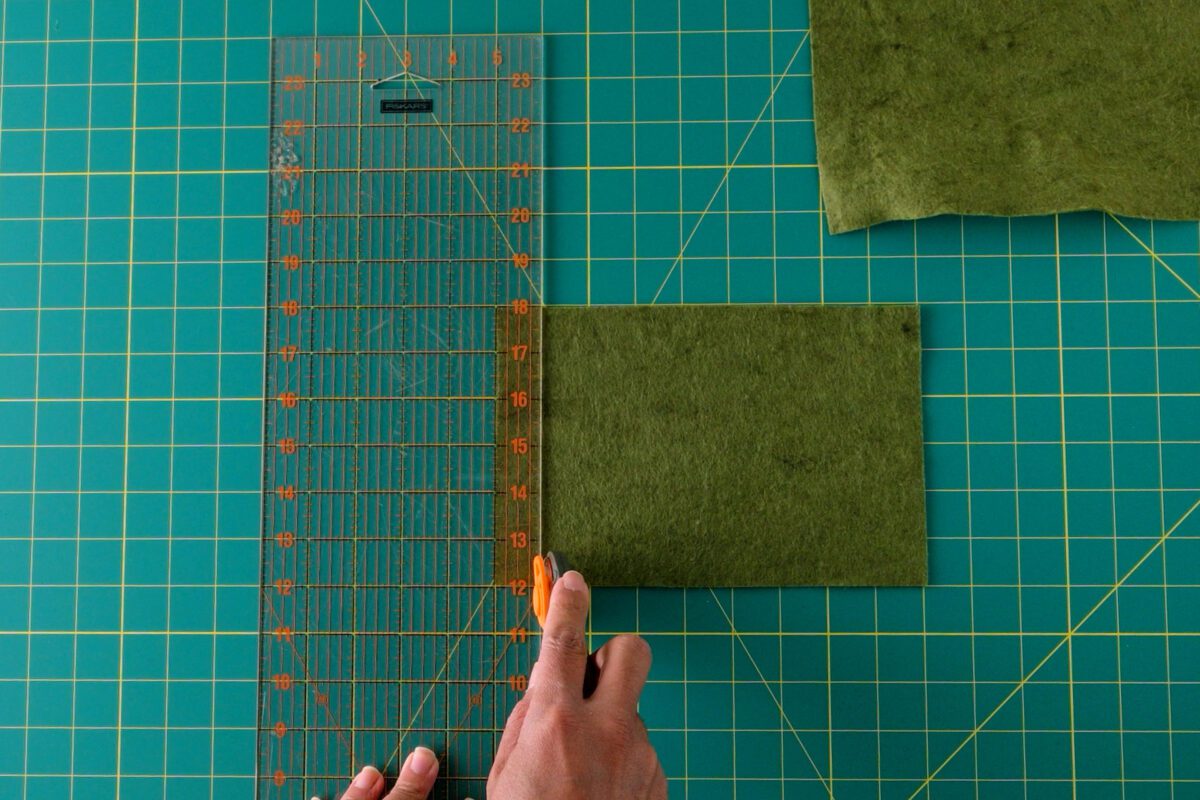 Cutting green felt sheet with Fiskars rotary cutter on gridded mat.