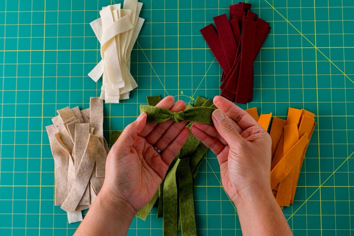 Hands tying a green felt strip to create a bow shape.