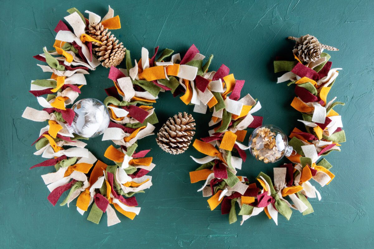 Decorated felt garland with pinecones and ornaments on green background.