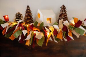 Felt garland on mantel with pinecone tree and lighted ceramic house.