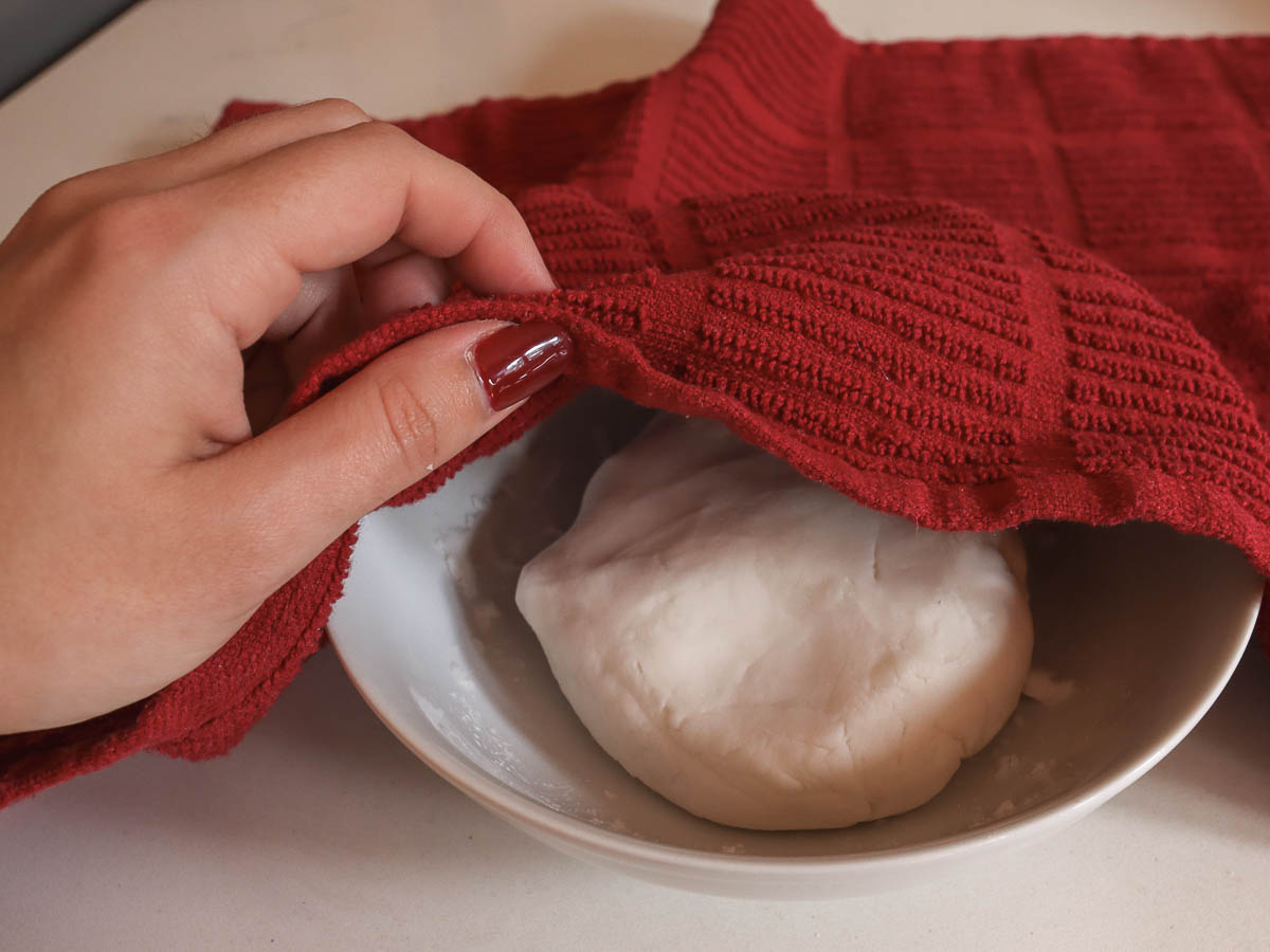 woman's hand lifting cloth covering dough