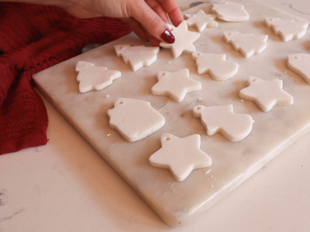 woman's hand placing a baking soda dough ornament on a marble board