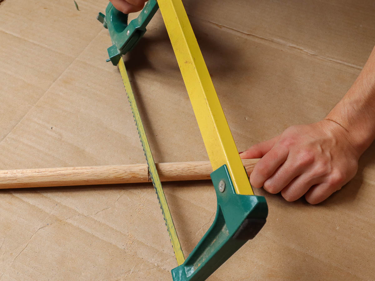 Woman's hands sawing wood dowel with hacksaw