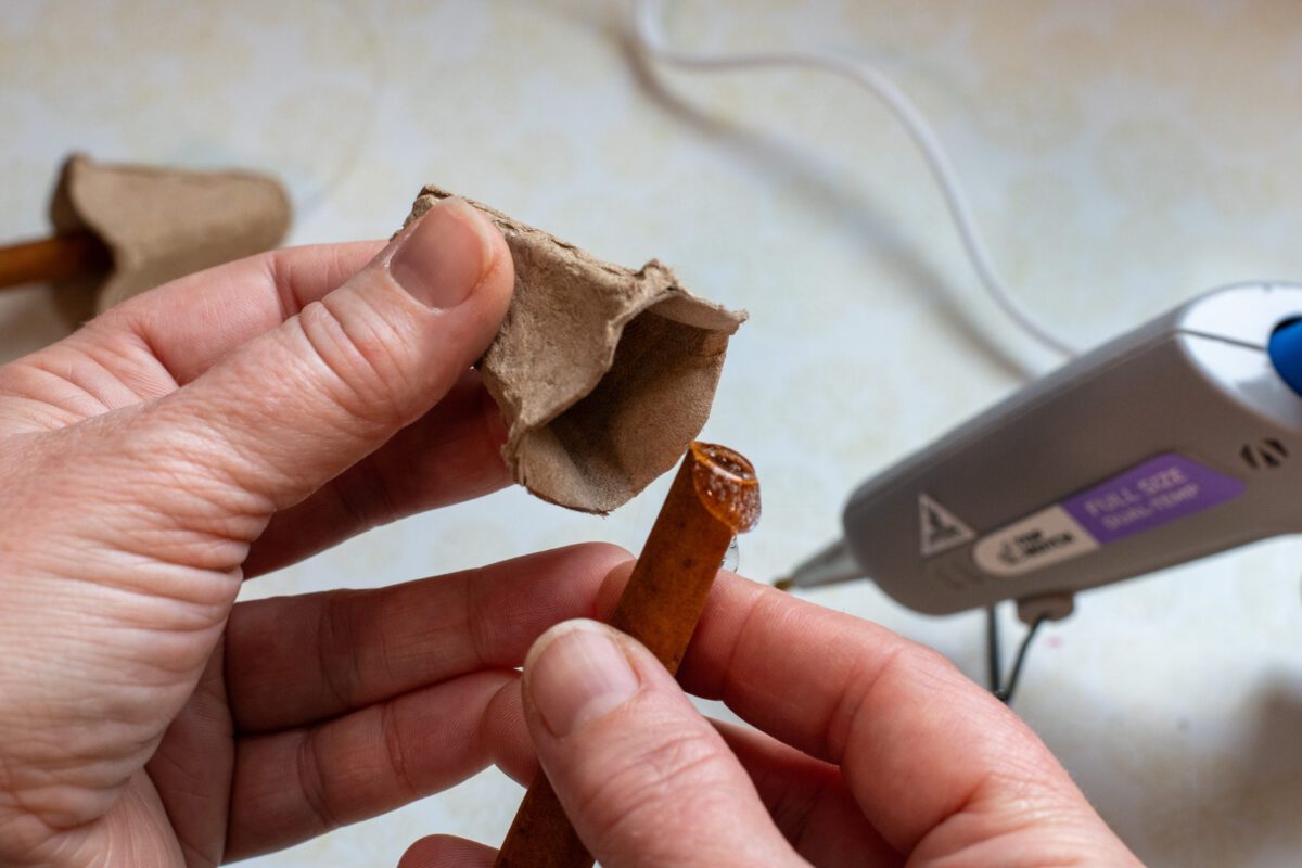 woman's hand gluing a cinnamon stick inside a cone from a paper egg carton